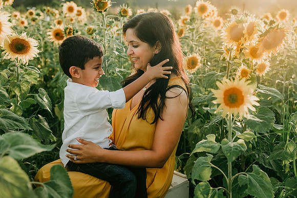pre school boy plays with his mother's hair while sitting amoung sunflowers at prospect farms