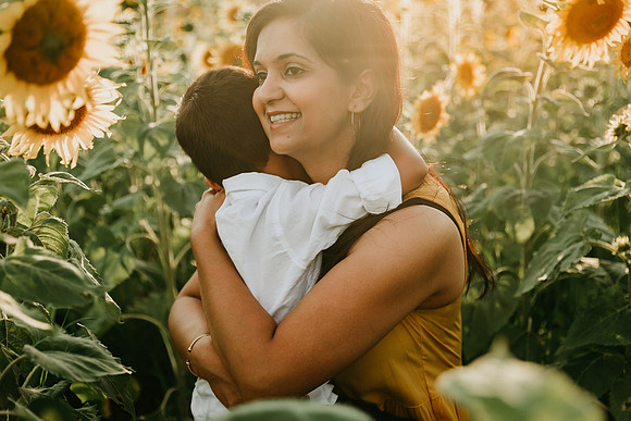 mother gets a hug from her pre school boy while sitting in a field of flowers by monica carlson photography