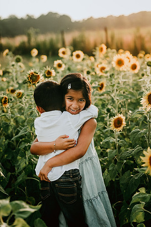 indian siblings hug each other while standing amound sunflowers by monica carlson photography
