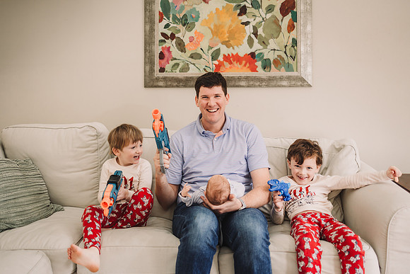 Dad holds newborn while playing with nerf guys with older boys