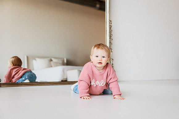 one year old girl crawls on a floor during a phot session with monica carlson