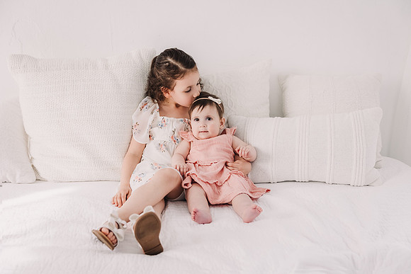 Big sister kisses little sisters head in a studio photo session