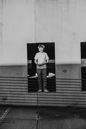 black and white image of a teen boy standing in the concrete frame of a parking lot