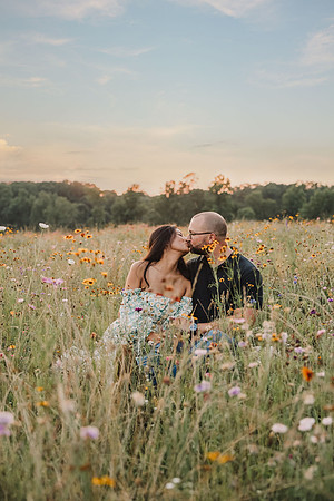 couple kiss while sitting in a flower field at sunset