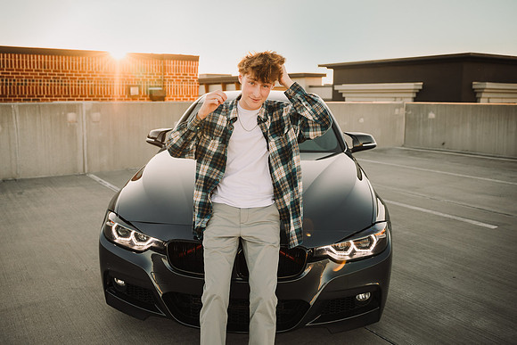 teen boy messes his hair while leaning on his car at sunset