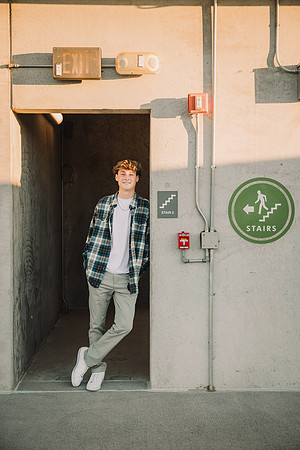 Lambert high school senior leans on a door frame under a Exit sign