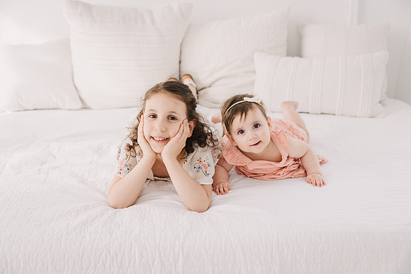 sister lay on a bed on their bellies