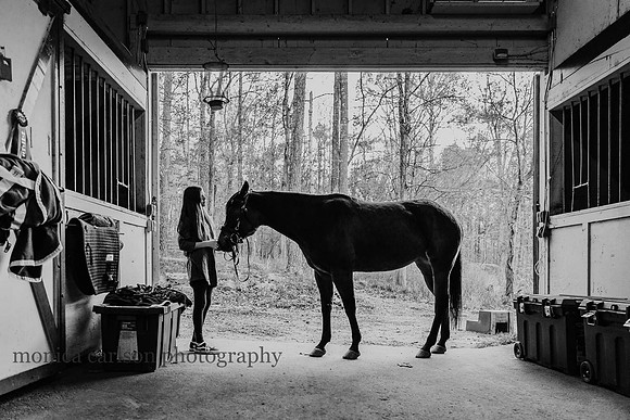 black and white image of a girl and her horse in a stable